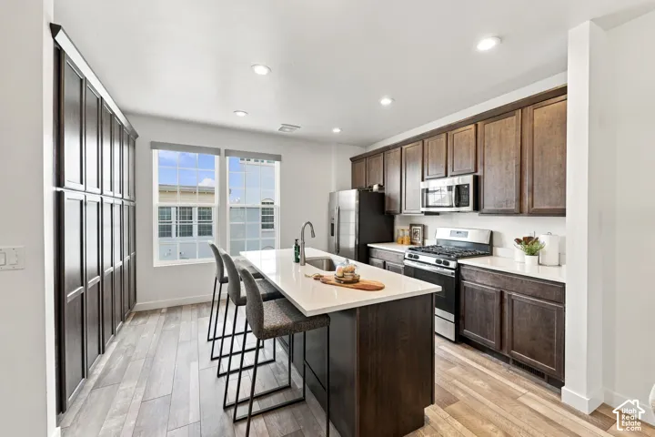Kitchen featuring dark wood-finish cabinetry, stainless steel appliances, a center island with countertop seating, recessed lighting, and wood-finish flooring