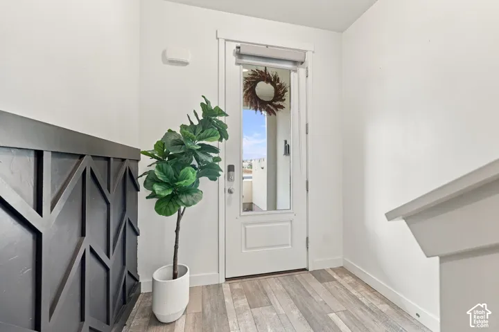 White entryway door with partial glass panel, wood-finish flooring, and white trim