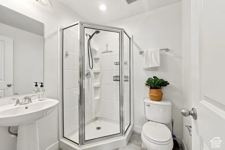 Pedestal sink, chrome fixtures, glass-enclosed shower, shower with built-in shelving, and light-toned tile flooring