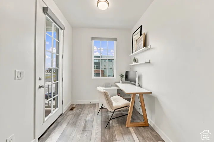 Bright interior with wood-finish flooring, a modern window, a door with multiple glass panes, and two wall-mounted shelves