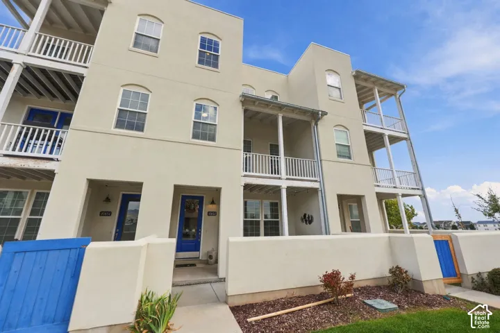 Multi-level exterior with stucco finish, multiple balconies with white railings, arched windows, and blue entry doors
