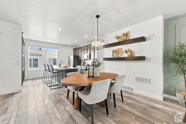 Open-concept dining area featuring wood-finish flooring, a contemporary chandelier, two floating shelves, and a paneled accent wall