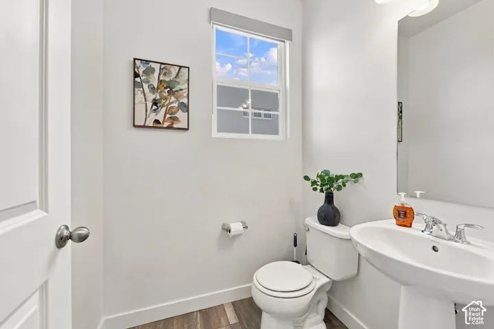 White wall paint with wood-finish flooring, a single window, and a pedestal sink with a chrome faucet