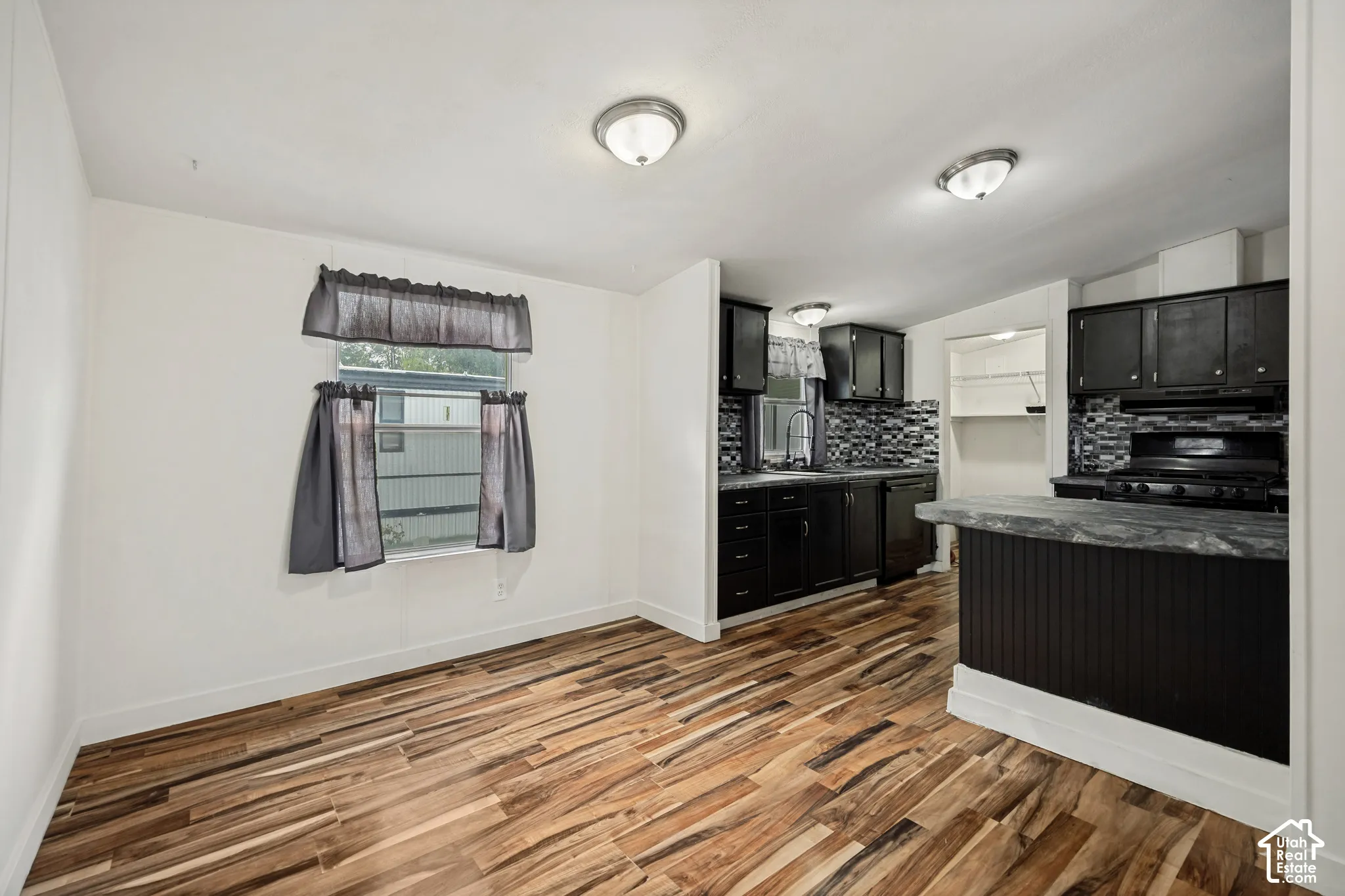 Updated kitchen with dark cabinetry, black appliances, textured tile backsplash, and wood-finish flooring