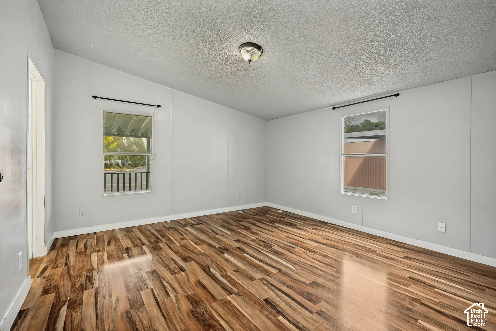 Wood-finish flooring, light gray walls, and two windows with dark curtain rods
