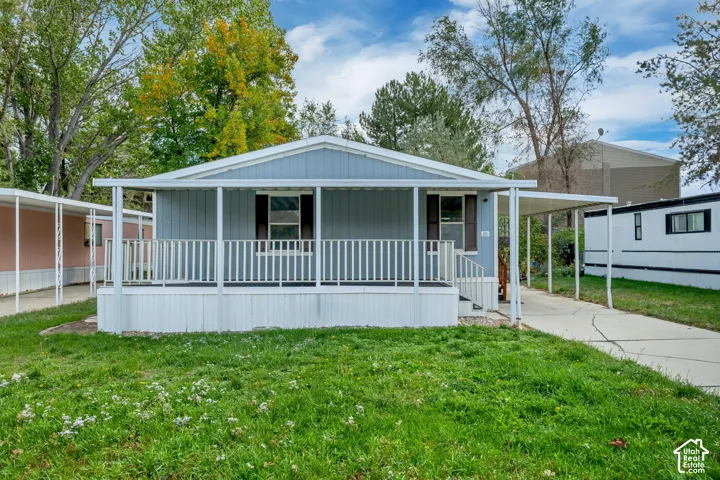 Light blue exterior with white trim, covered front porch, white porch railing, front steps, and a paved driveway with a carport