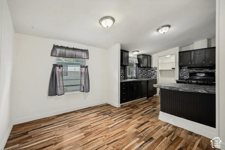 Updated kitchen with dark cabinetry, black appliances, textured tile backsplash, and wood-finish flooring