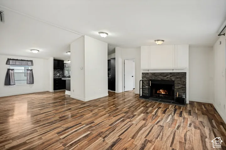 Wood-finish flooring, stone-faced fireplace with white mantel, white walls, and recessed lighting