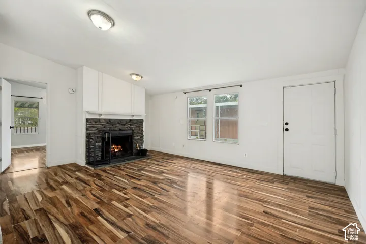 Wood-finish flooring, stone-clad fireplace with mantel, white walls, and built-in ceiling lighting