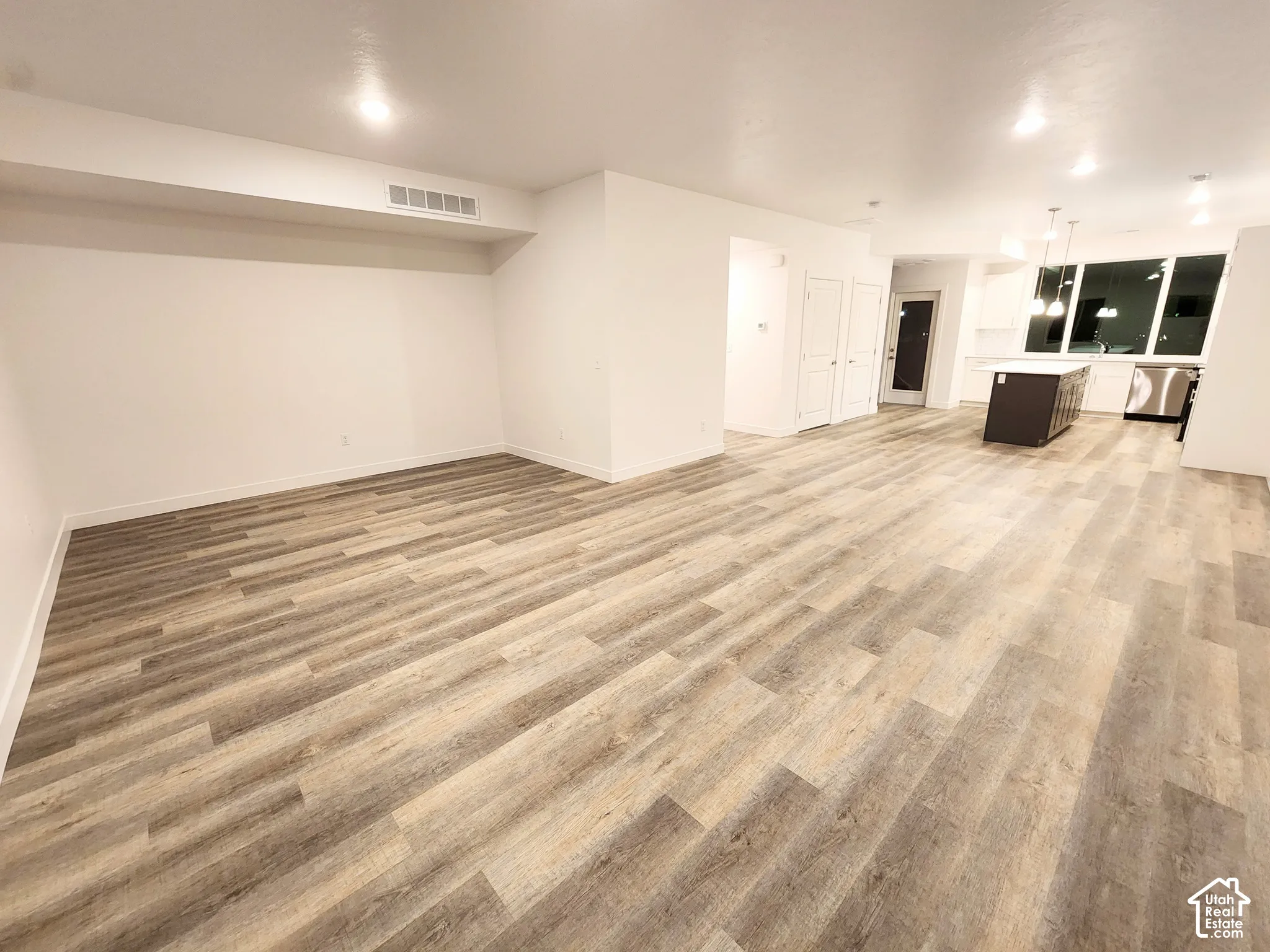 Open floor plan featuring wood-finish flooring, recessed ceiling lighting, kitchen island with countertop, and large windows
