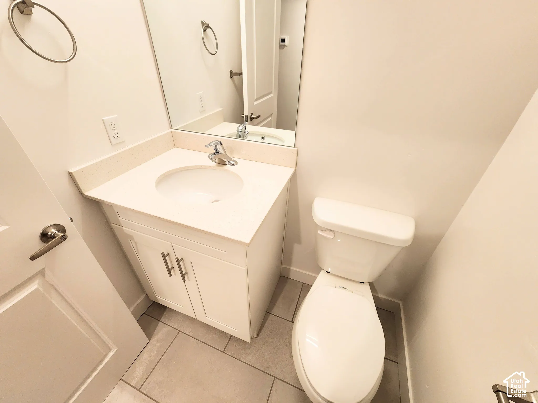 Vanity featuring a stone-composite countertop, undermount sink with a polished chrome faucet, white cabinetry with silver-tone hardware, large wall-mounted mirror, and tile flooring