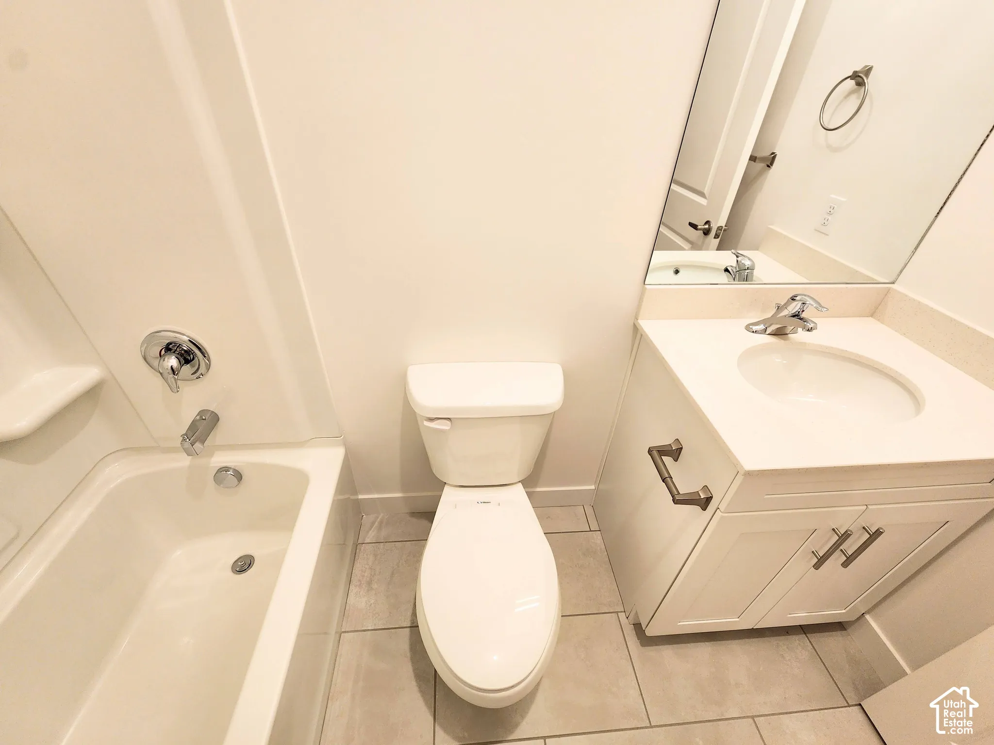 Full bathroom featuring a tub-shower combination with a chrome fixture, white vanity cabinet with an integrated sink, polished countertop, and neutral-toned tile flooring