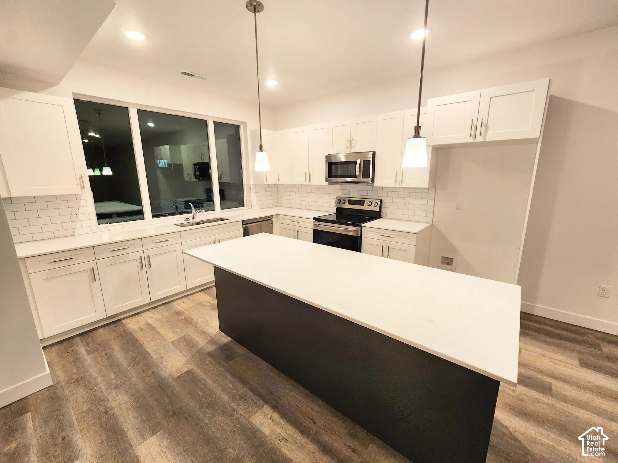 Kitchen featuring white shaker-style cabinetry, quartz countertops, a central island with a contrasting dark base, subway tile backsplash, and wood-finish flooring