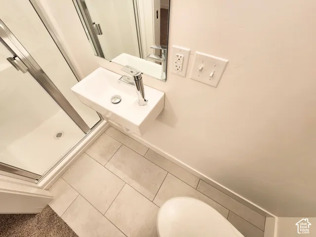 Wall-mounted rectangular basin with a single-handle faucet, frameless glass shower enclosure, and large-format tile flooring