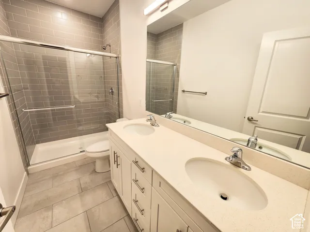 Double vanity featuring a light-toned solid surface countertop with dual undermount sinks, white cabinetry with metallic hardware, oversized frameless mirror, and a walk-in shower with grey subway tile surround