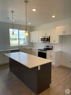 Kitchen featuring white shaker-style cabinetry, an expansive center island with a stone-finish countertop, subway tile backsplash, stainless steel appliances, and wood-finish flooring