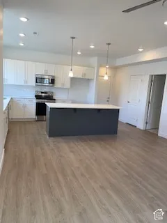 Kitchen featuring white cabinetry, contrasting dark-toned central island with a stone-finish countertop, wood-finish flooring, subway tile backsplash, and stainless steel appliances