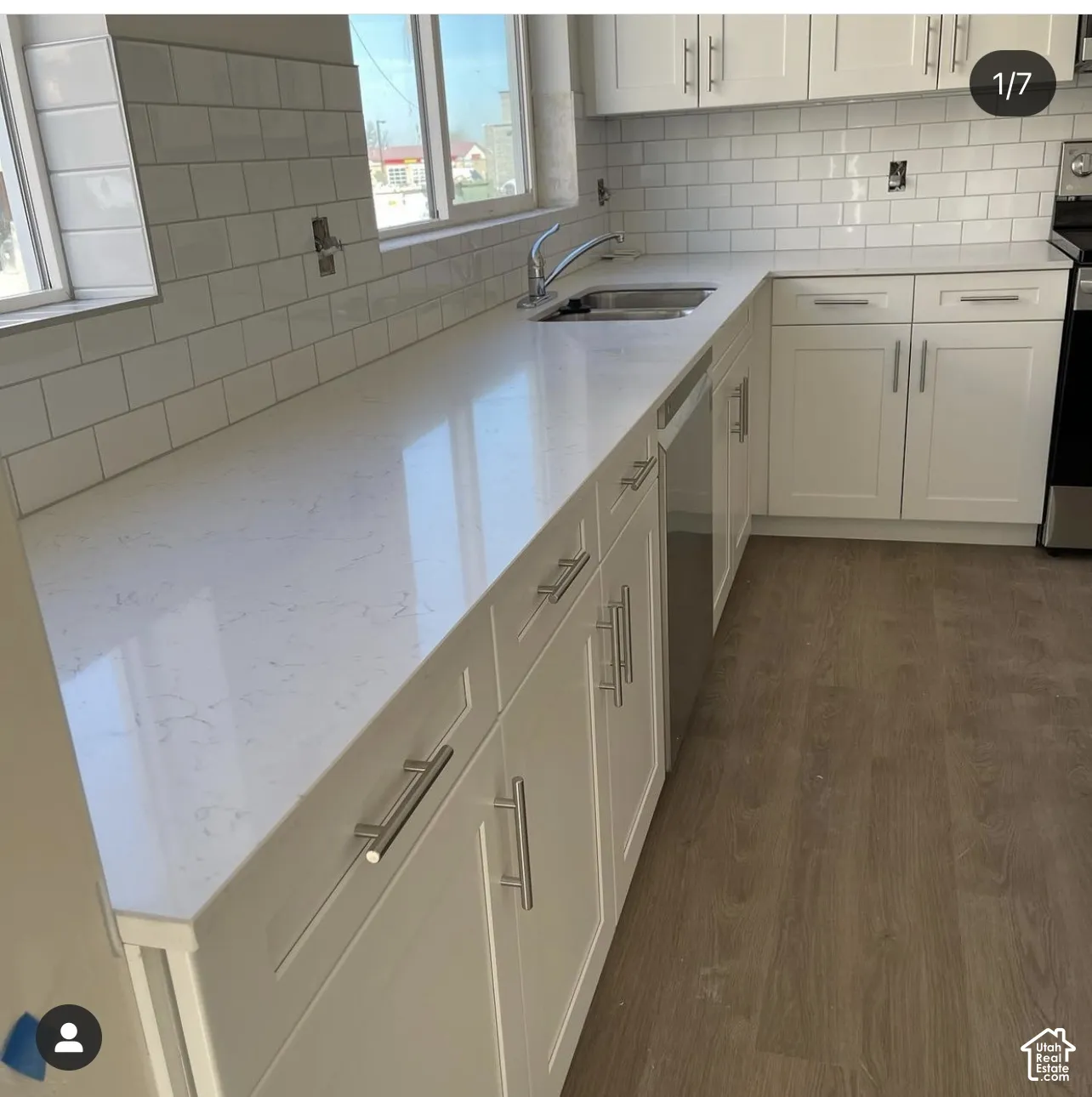 Kitchen featuring white cabinetry with stainless steel hardware, solid-surface countertops, white subway tile backsplash, stainless steel under-mount sink, and wood-finish flooring