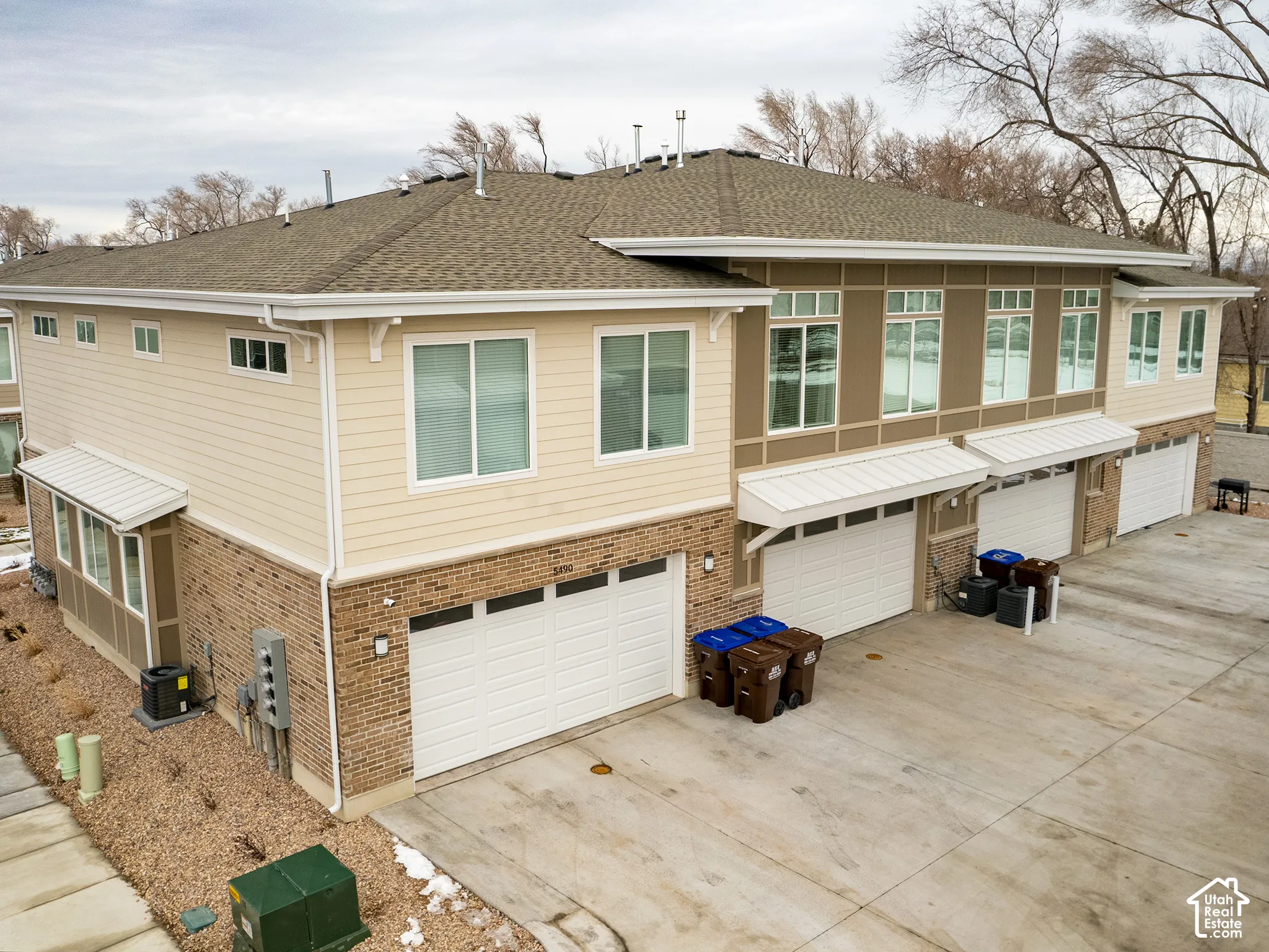 Multi-unit exterior featuring mixed brick and horizontal siding, composite shingle roof, metal window awnings, and multi-car garage access