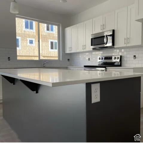 Kitchen featuring a contrasting dark-toned island with a stone-composite countertop, white shaker-style cabinetry, white subway tile backsplash, and stainless steel built-in appliances