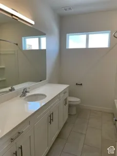 Bathroom featuring a white vanity with a light-toned solid surface countertop, an integrated sink, a full-width mirror with an integrated light fixture, and tile flooring