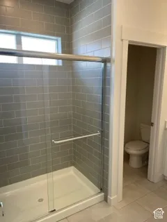 Walk-in shower featuring grey subway tile surround, frameless glass sliding enclosure, and a built-in window, complemented by large-format floor tile
