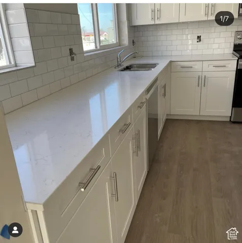Kitchen featuring white cabinetry with stainless steel hardware, solid-surface countertops, white subway tile backsplash, stainless steel under-mount sink, and wood-finish flooring