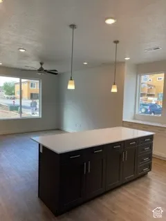 Kitchen island featuring dark cabinetry, a light-toned solid surface countertop, wood-finish flooring, recessed lighting, and dual pendant fixtures