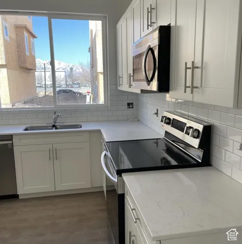 Kitchen featuring white shaker-style cabinetry, quartz countertops, white subway tile backsplash, stainless steel appliances, and wood-finish flooring