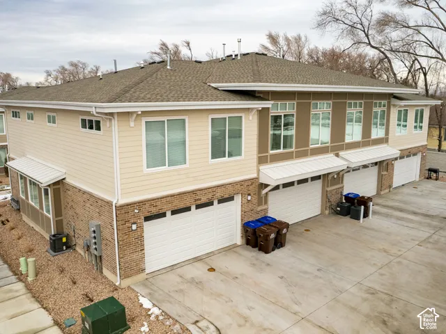 Multi-unit exterior featuring mixed brick and horizontal siding, composite shingle roof, metal window awnings, and multi-car garage access