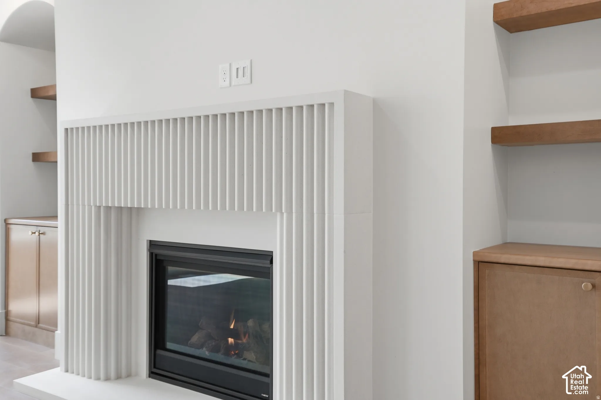 Fireplace featuring a fluted white surround, integrated wood-finish cabinetry, and recessed floating wood-finish shelving