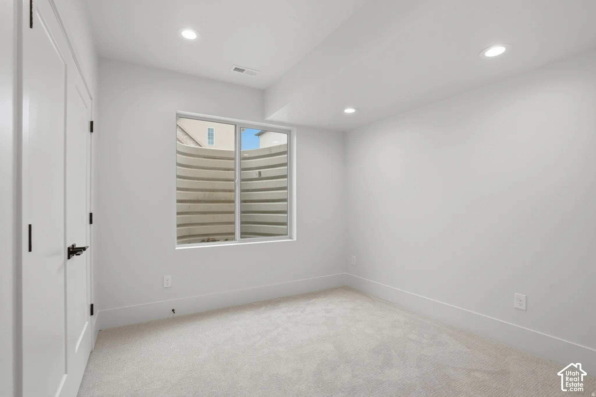 Neutral-toned carpeted flooring, inset ceiling lighting, and a slider window featuring a corrugated window well