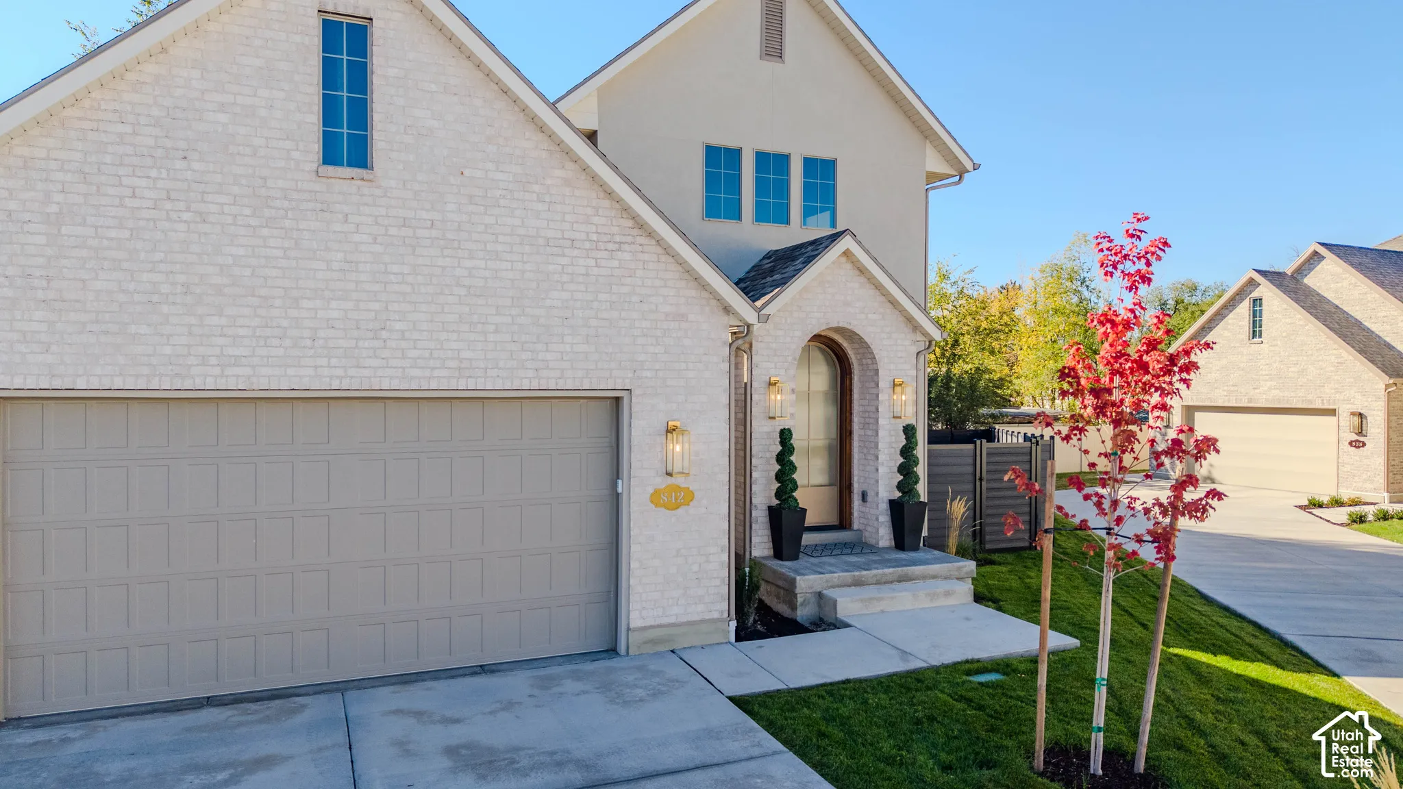 Light-colored brick facade, arched entryway, attached two-car garage, concrete driveway, and covered porch steps