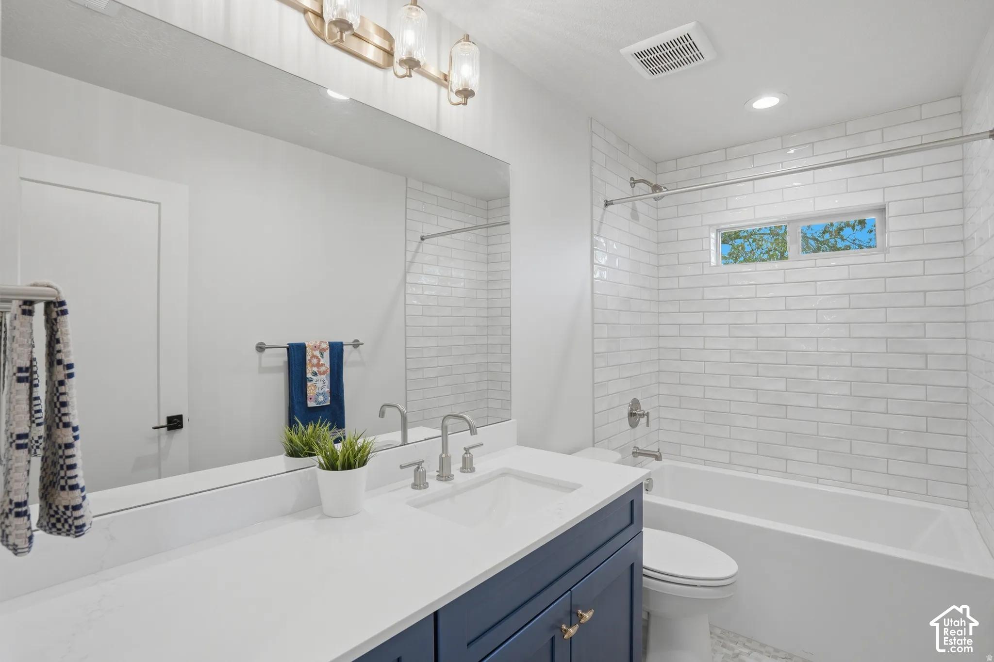 Bathroom featuring a navy blue vanity with a white countertop, undermount sink, brushed nickel hardware, and a white subway-tile shower surround