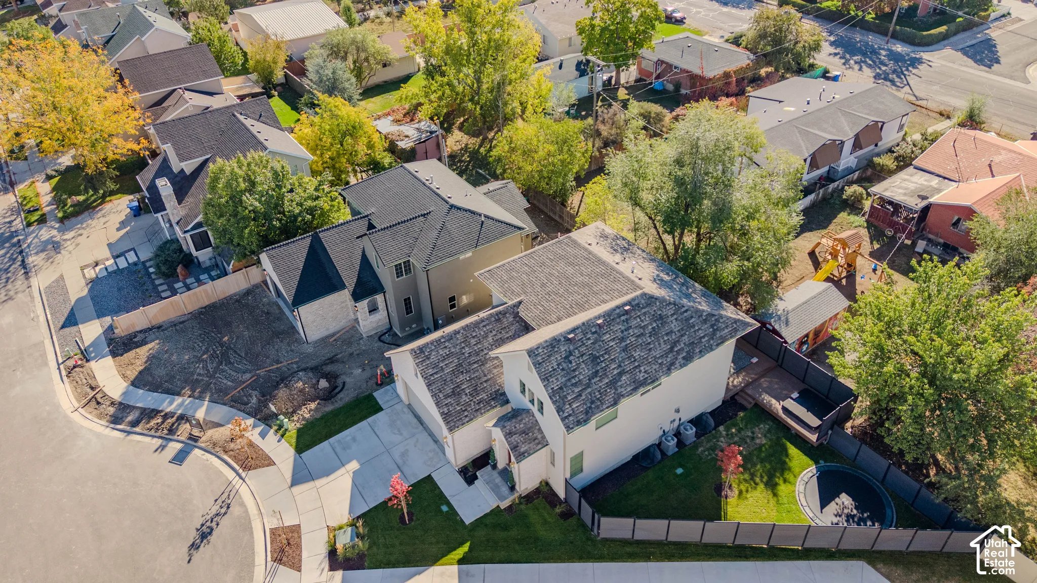 Aerial view of the property featuring a multi-level residence, attached multi-car garage, concrete driveway, and enclosed backyard with mature trees