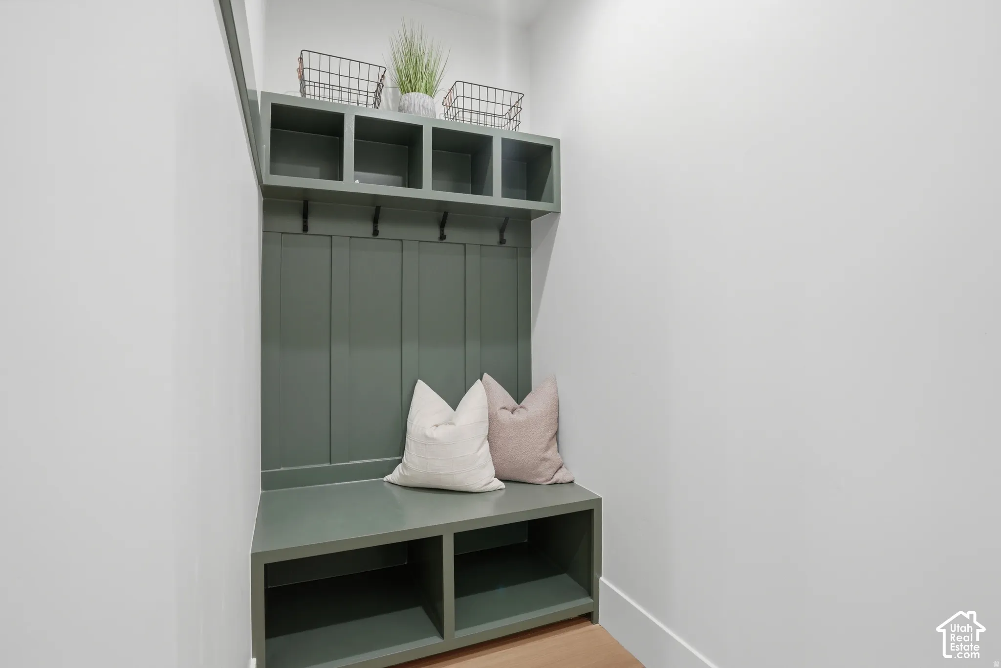 Built-in mudroom storage featuring green cabinetry, board-and-batten paneling, overhead cubbies, integrated wall hooks, and a bench with lower open shelving