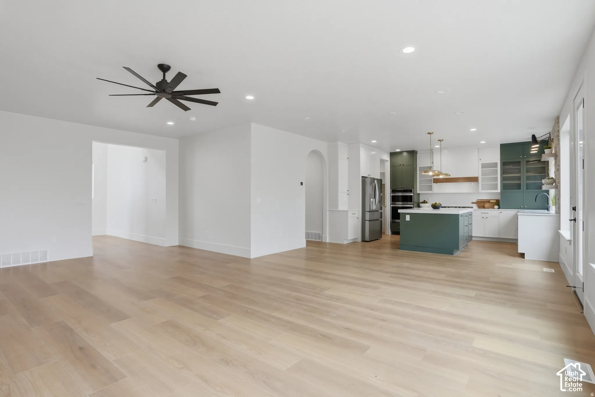 Open-concept interior featuring wood-finish flooring, recessed lighting, multi-blade ceiling fan, arched doorway, and kitchen with contrasting cabinetry and central island