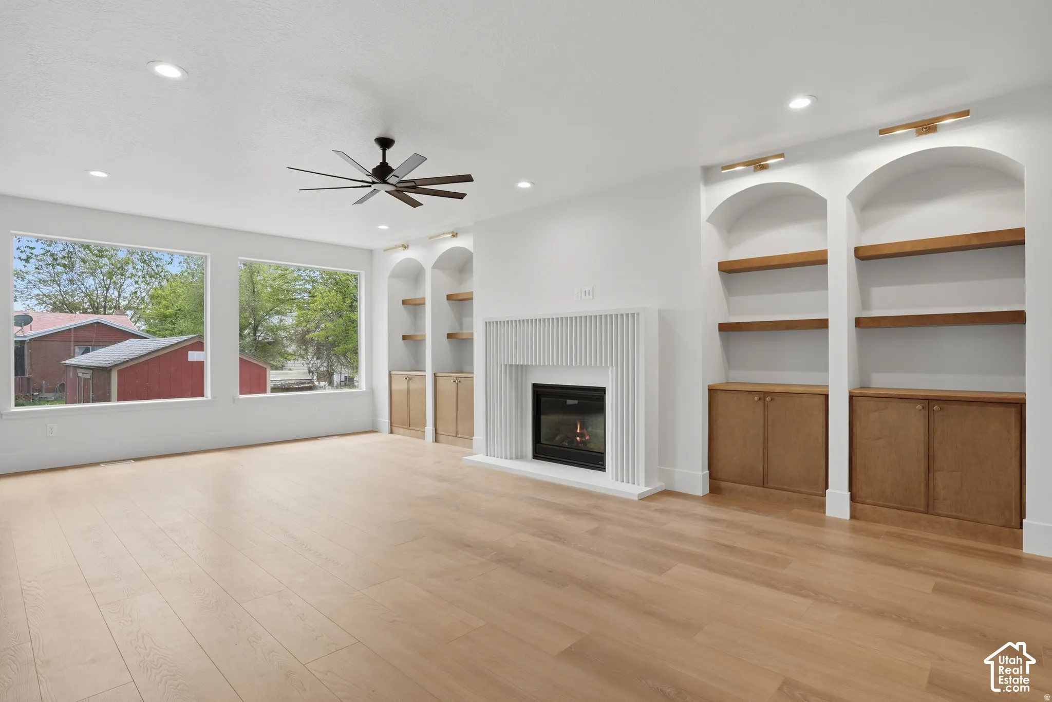 Living area featuring wood-finish flooring, recessed lighting, a fireplace with a fluted surround, and arched built-in cabinetry with wood shelving