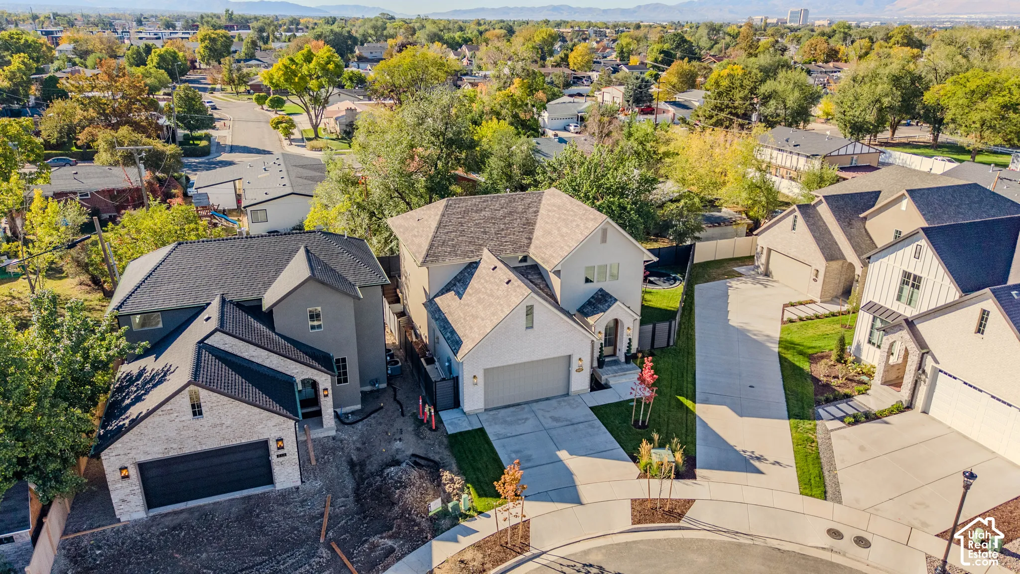 Aerial perspective of a multi-level suburban residence featuring a multi-gabled roofline, light-toned exterior siding, attached multi-car garage, and concrete driveway