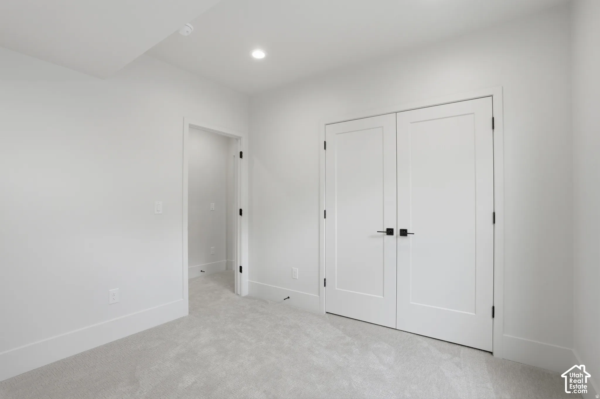 Neutral-toned carpeting, white shaker-style double doors, matte black hardware, recessed ceiling lighting, and smooth wall finish