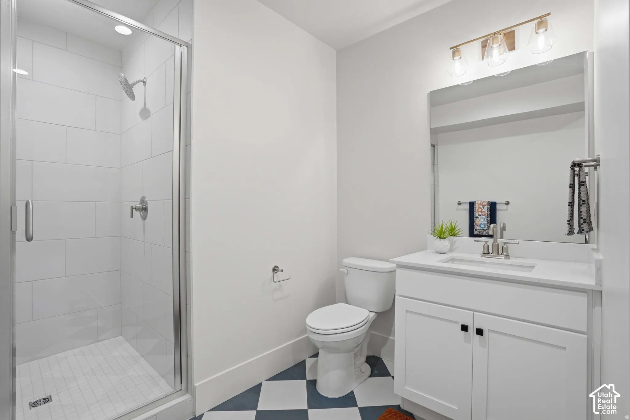 Bathroom featuring a walk-in shower with subway-style tile, vanity with a white countertop and integrated sink, chrome faucet fixtures, and geometric-patterned floor tile