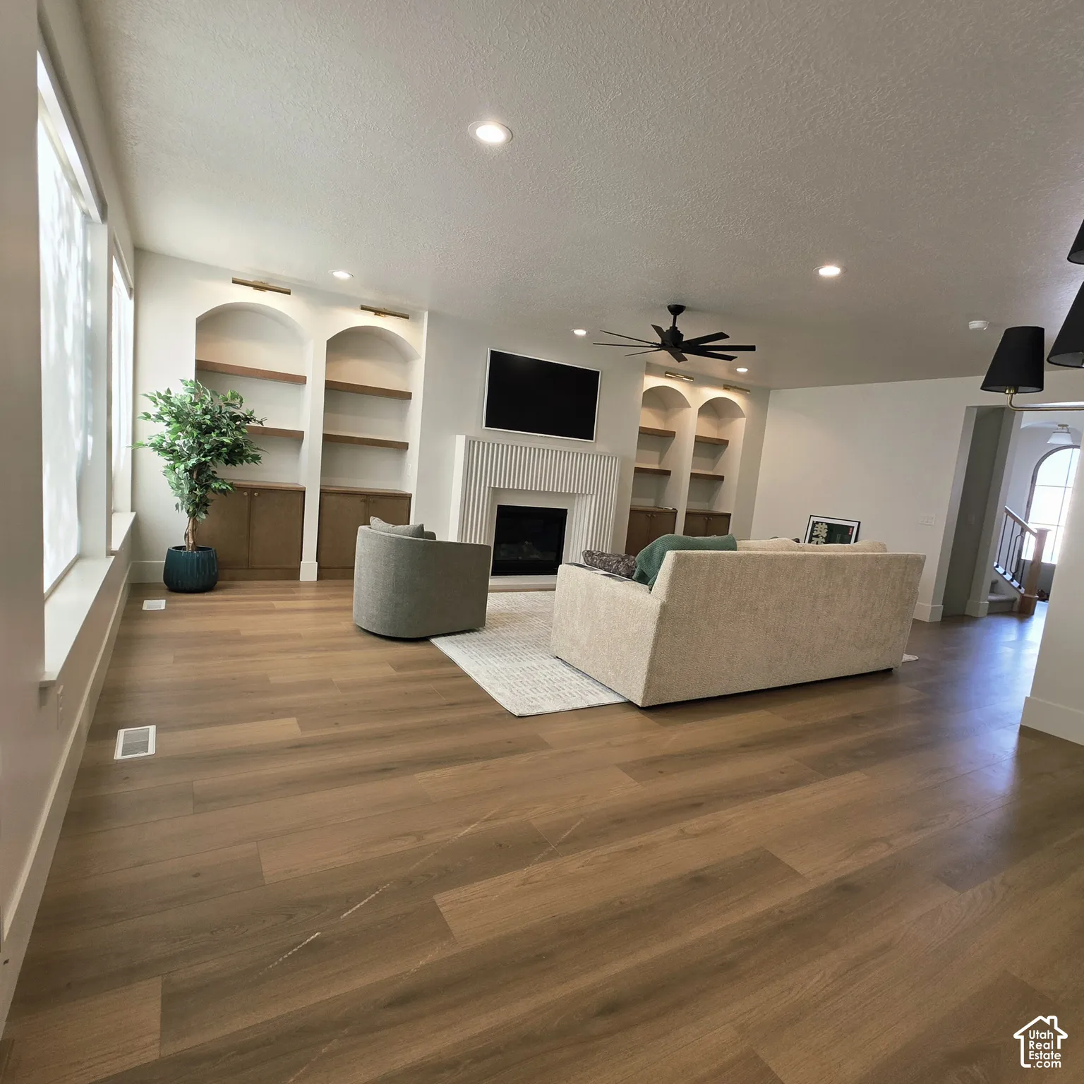 Living room featuring wood-finish flooring, recessed lighting, a fireplace with a fluted surround, and custom built-in arched shelving with cabinet storage