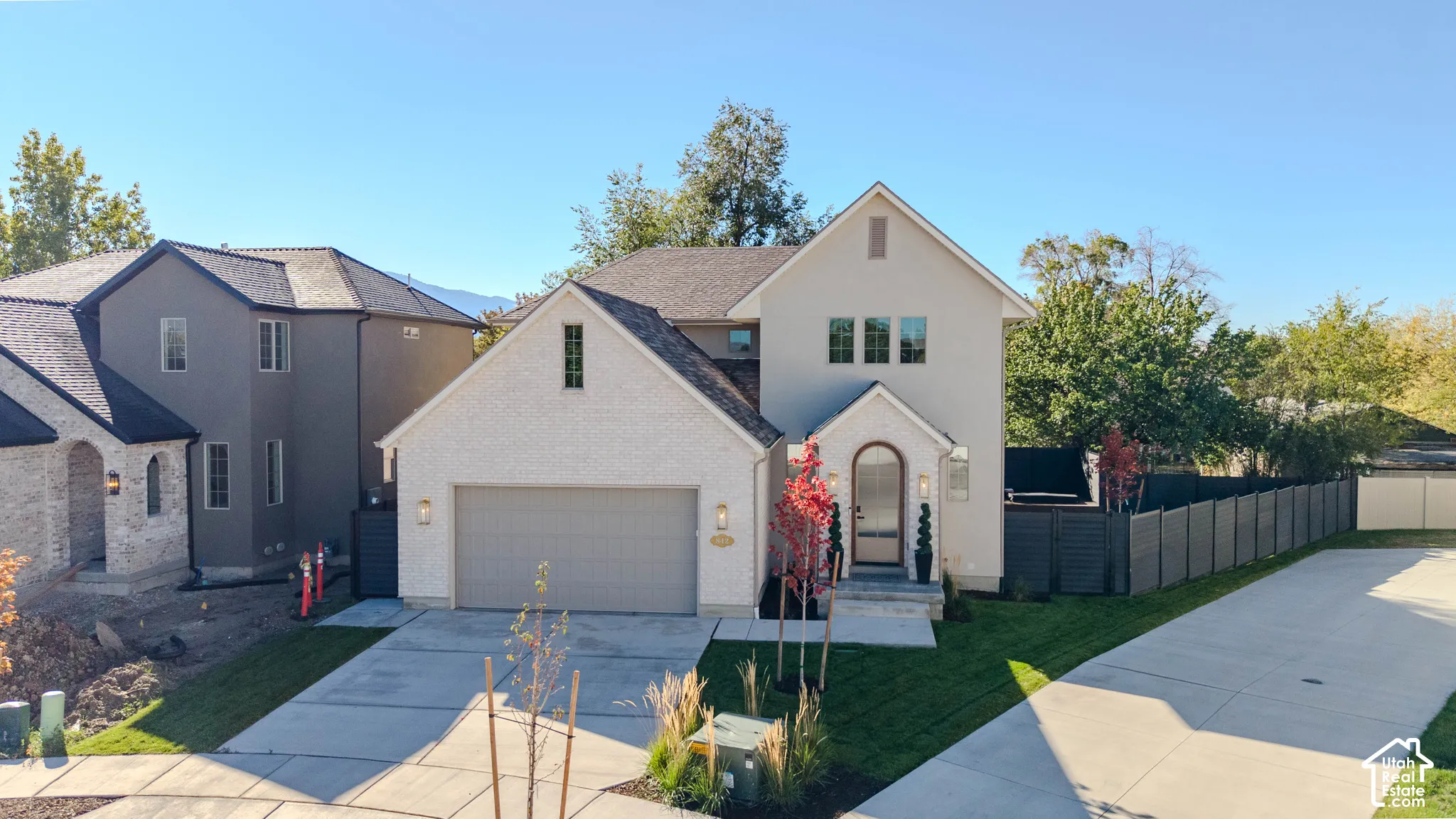 Multi-story exterior featuring a brick and stucco facade, an attached two-car garage, arched front entryway, and a concrete driveway