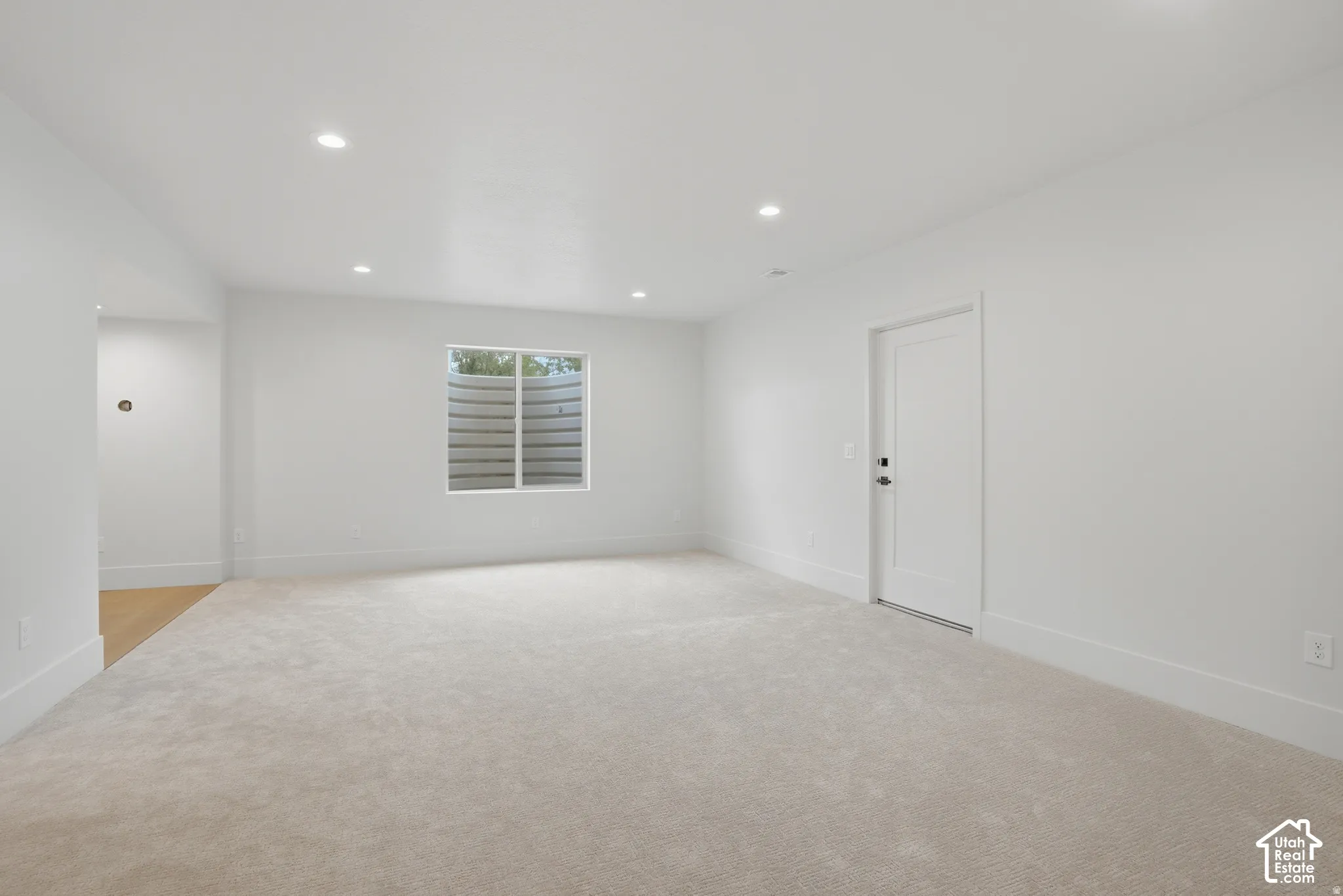 Neutral-toned interior space featuring recessed ceiling lighting, wall-to-wall carpeting, a window with an integrated egress well, and a paneled door