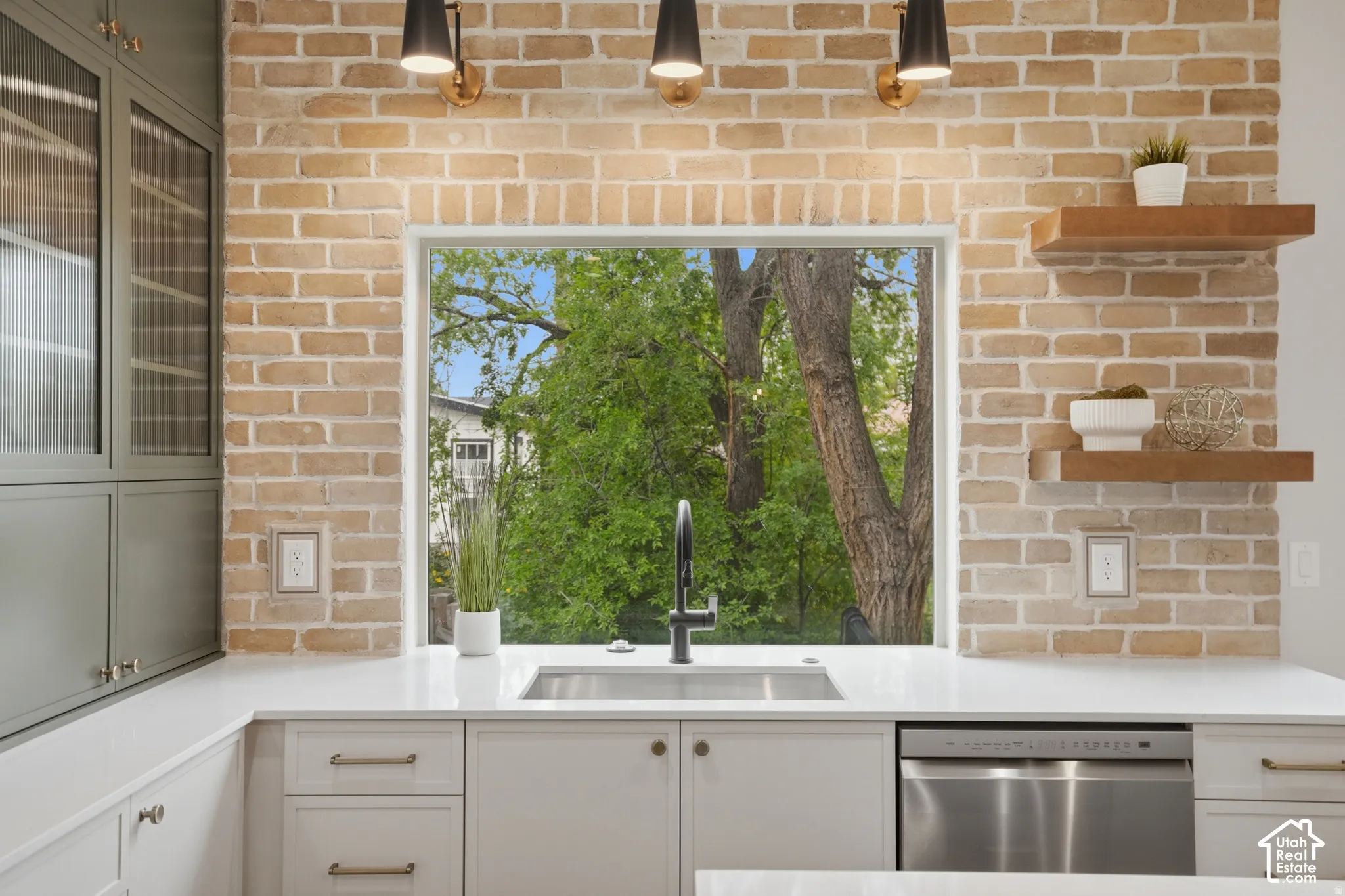 Exposed brick accent wall with a large picture window, undermount stainless steel sink, matte black gooseneck faucet, quartz countertops, and floating wood shelving
