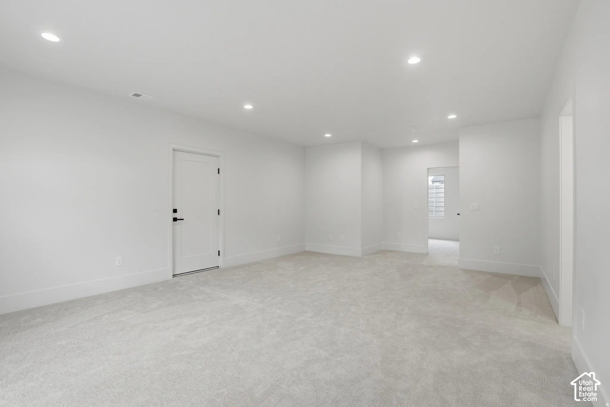 Neutral interior featuring plush wall-to-wall carpeting, recessed ceiling lighting, and a solid-core interior door with matte black hardware