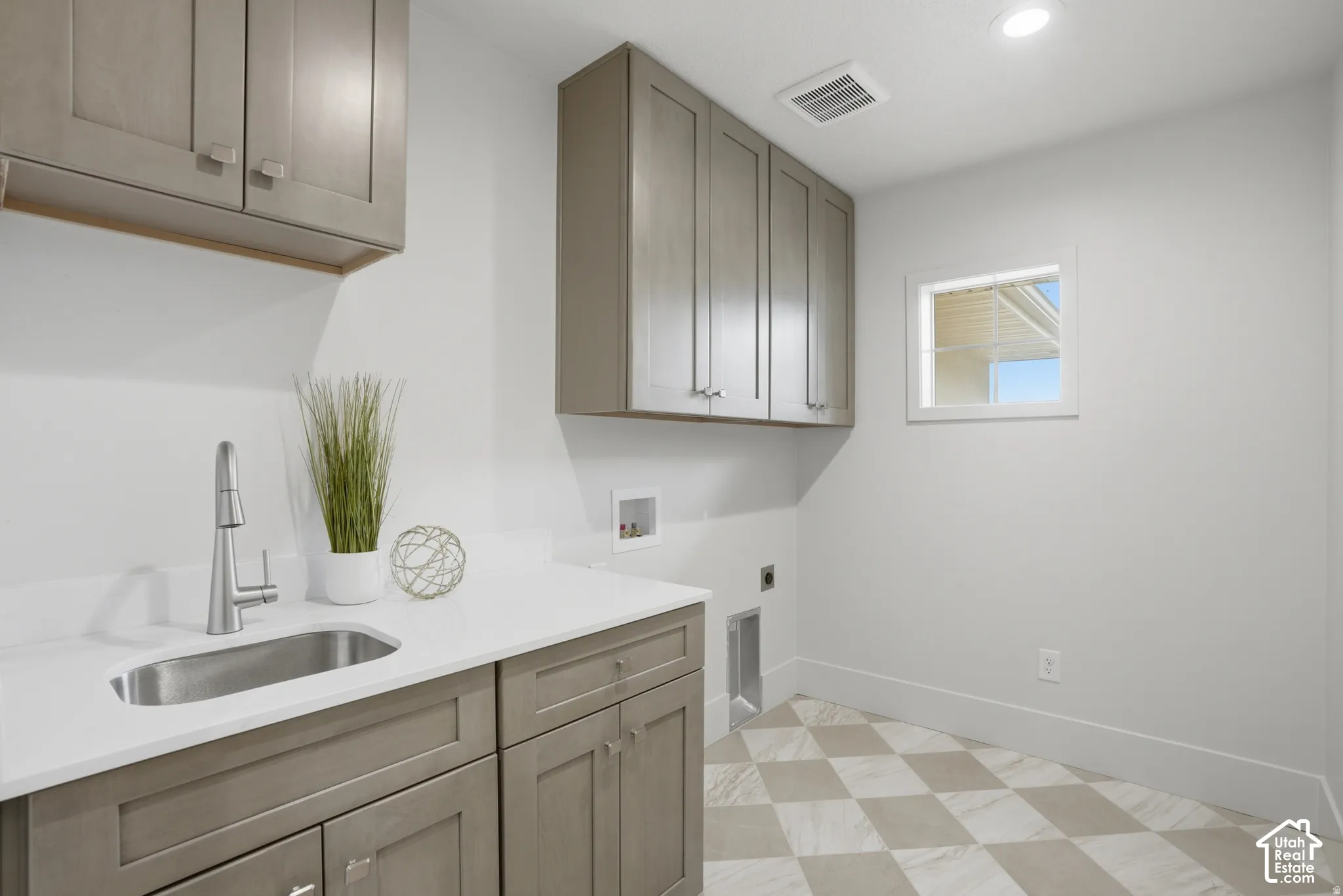 Laundry area featuring grey shaker-style cabinetry, quartz countertops, a stainless steel undermount sink with a high-arch faucet, and diamond-patterned tile flooring