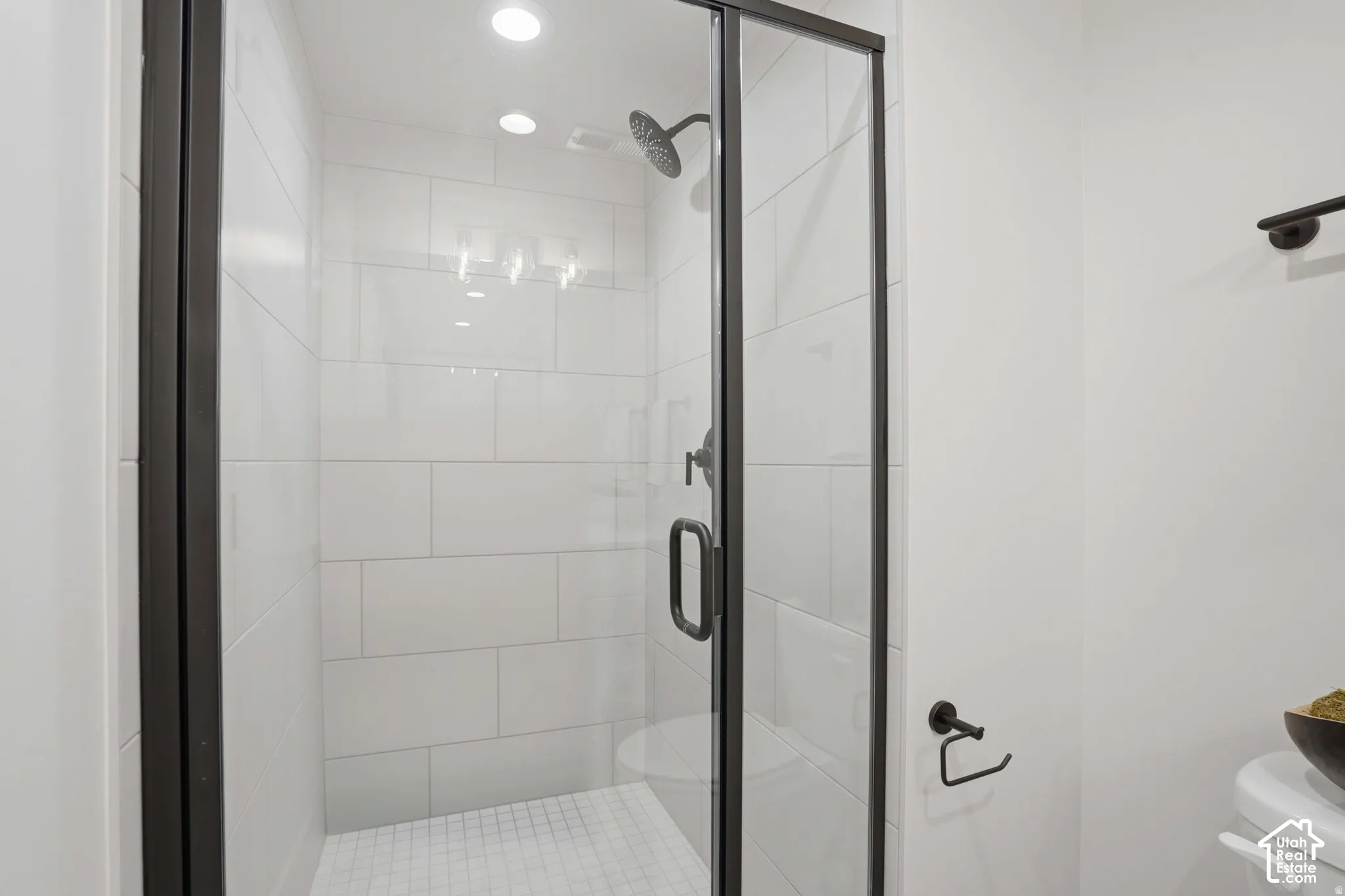 Walk-in shower featuring large-format white tile, matte black hardware, a rainfall shower head, and a glass enclosure with a black metal frame