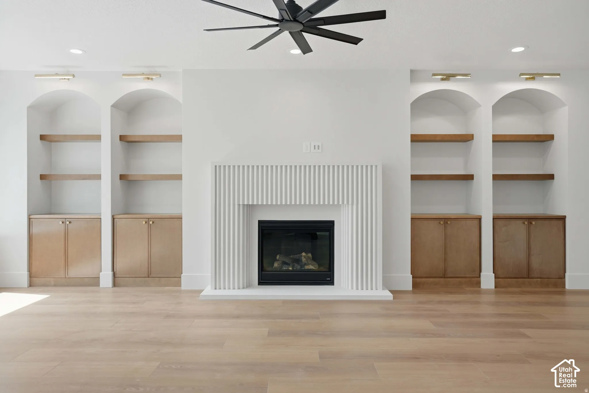 Fireplace featuring a fluted surround, flanked by custom cabinetry with arched recessed shelving and wood-finish lower storage, recessed ceiling lighting, and a multi-blade ceiling fan