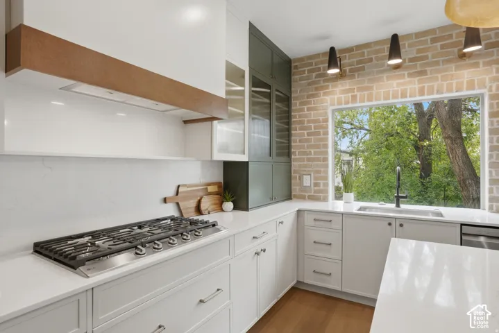 Kitchen featuring white quartz countertops, custom two-tone cabinetry with glass-front uppers, a built-in gas cooktop, a statement exposed brick wall, and a stainless steel under-mount sink